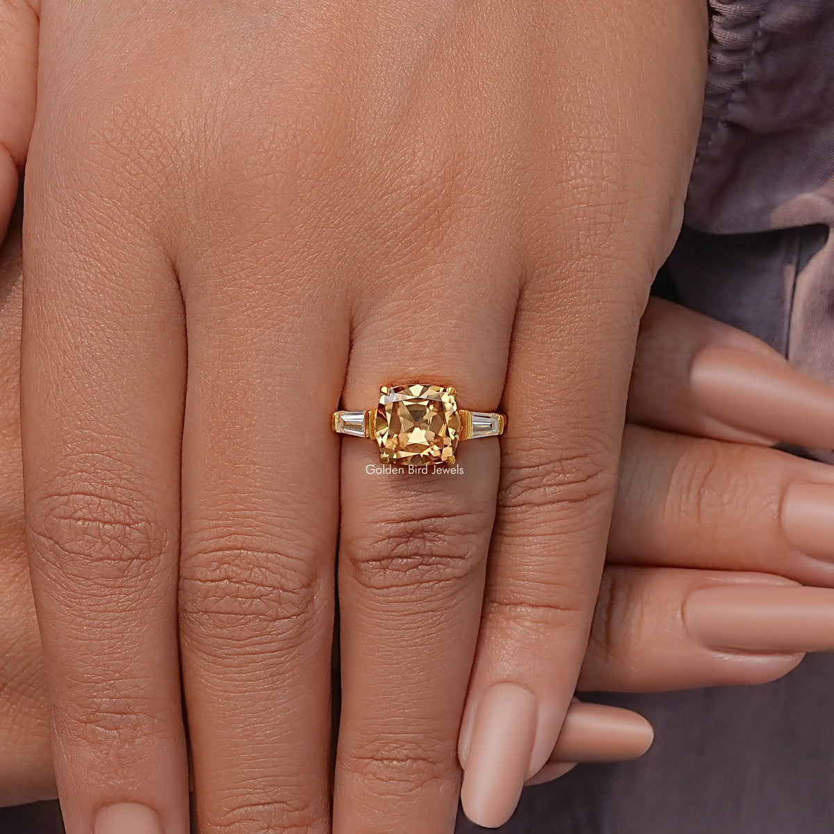 Gold three-stone ring with cushion center stone and baguette side stones, on hand