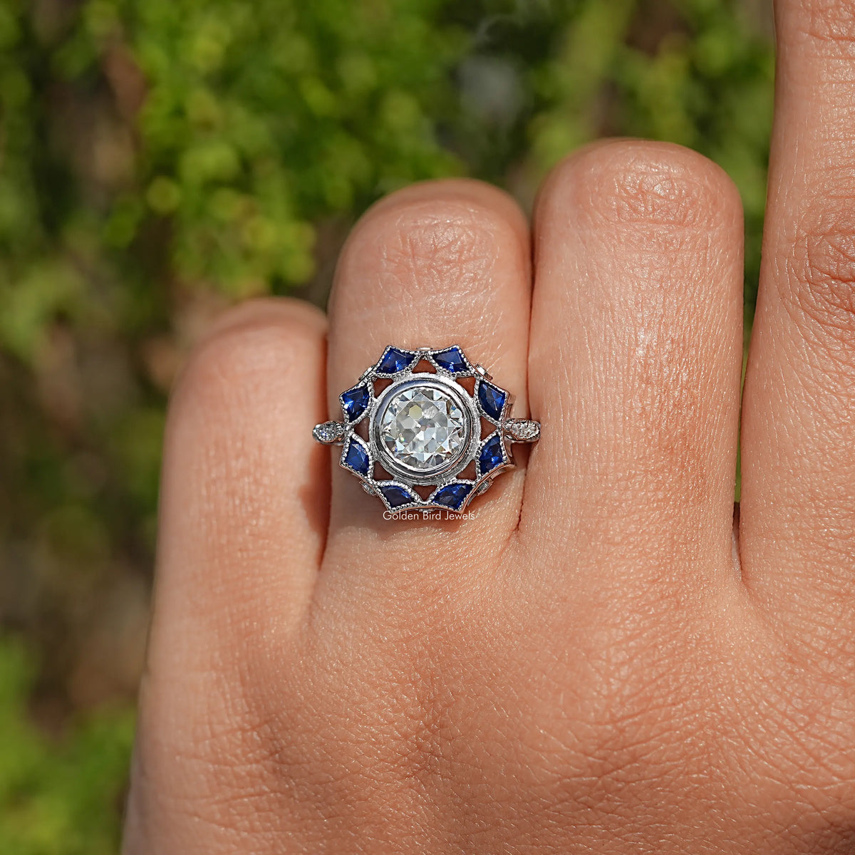 Round moissanite and blue halo ring on finger with a silver prong-set band