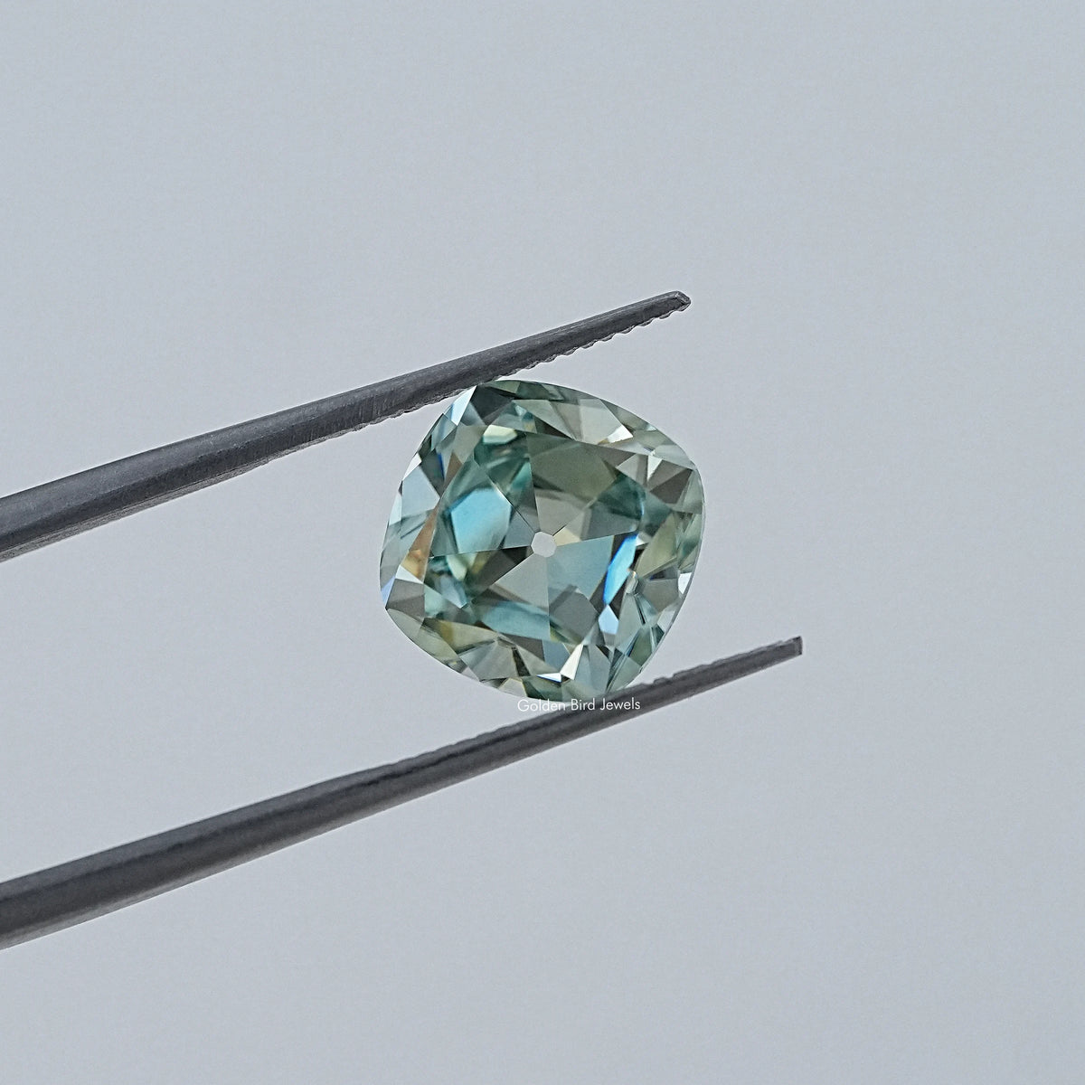 Faceted cushion-cut moissanite gemstone in tweezers, light blue