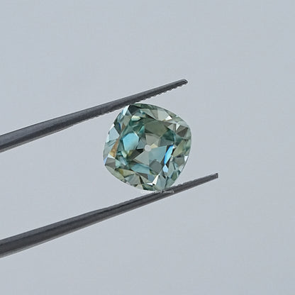 Faceted cushion-cut moissanite gemstone in tweezers, light blue