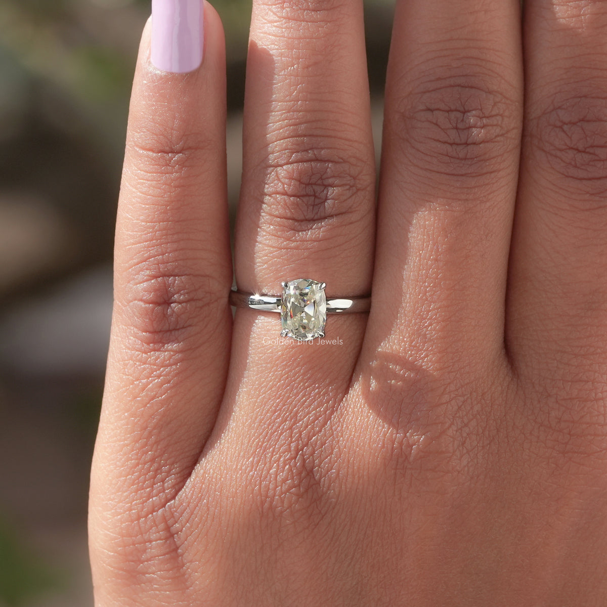 Silver solitaire moissanite ring on finger, cushion-cut center stone in prongs