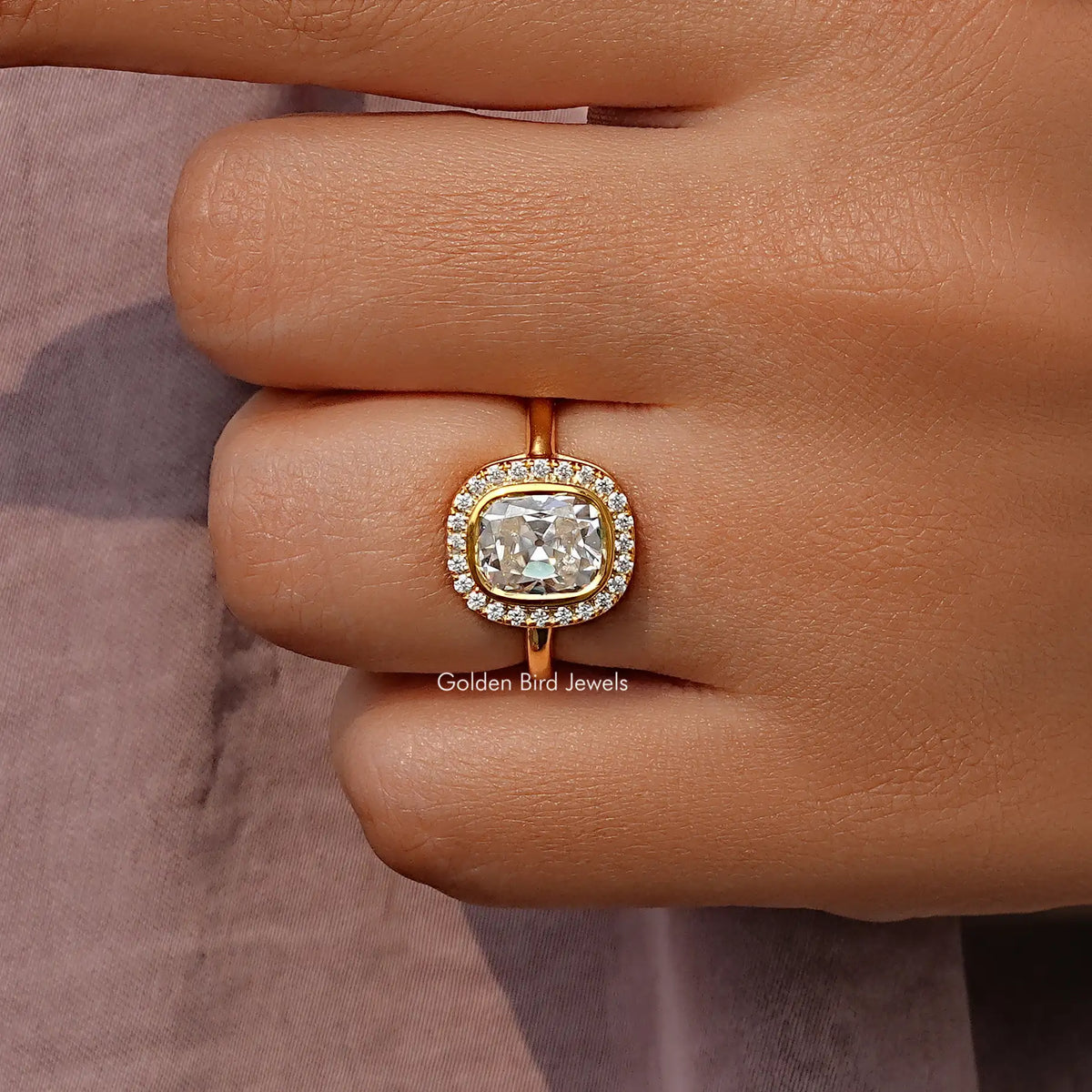 Cushion-cut moissanite halo ring in gold-tone setting on a finger