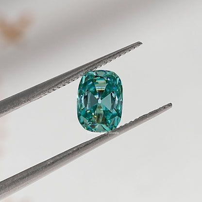 Blue-green cushion-cut moissanite gemstone held in tweezers, close-up facet view.