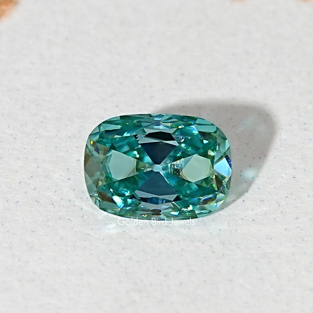 Blue-green cushion-cut moissanite gemstone loose and centered, front-facing faceted view.