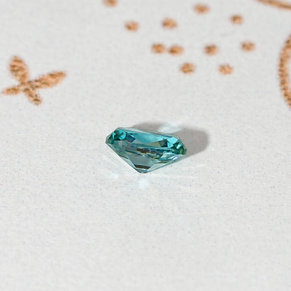 Blue-green cushion-cut moissanite gemstone shown at an angle, loose faceted stone.