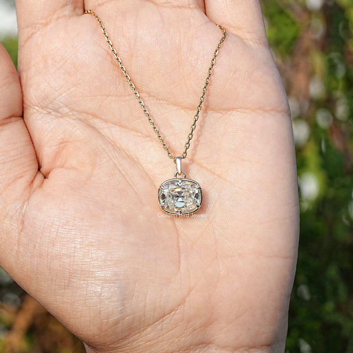 Cushion-cut moissanite pendant on gold chain held in open palm