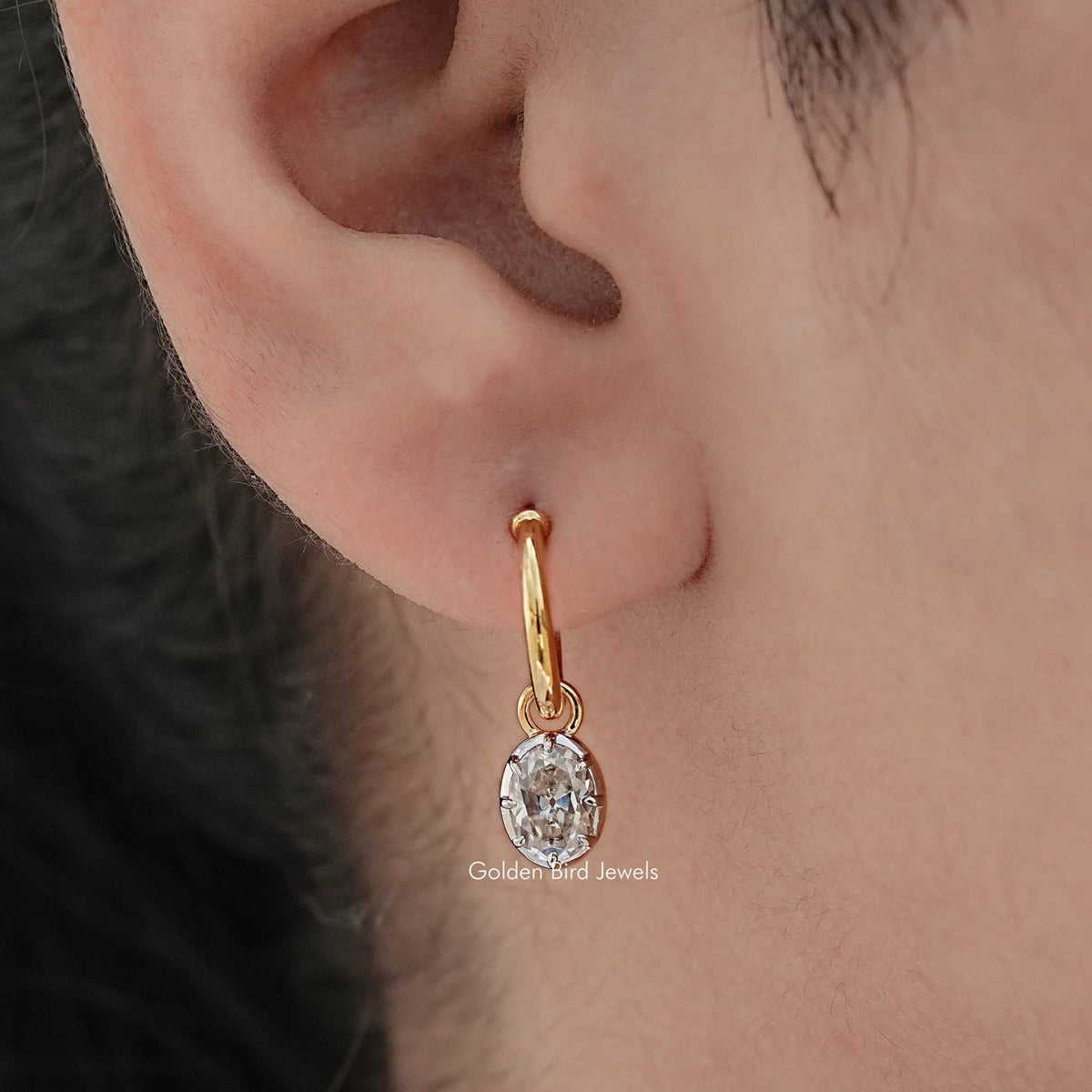Gold-tone hoop dangle earring with oval-cut moissanite stone, ear close-up