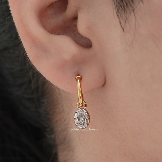 Gold-tone hoop dangle earring with oval-cut moissanite stone, ear close-up