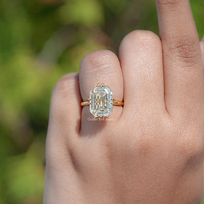 Gold-tone solitaire engagement ring on finger with emerald-cut clear stone