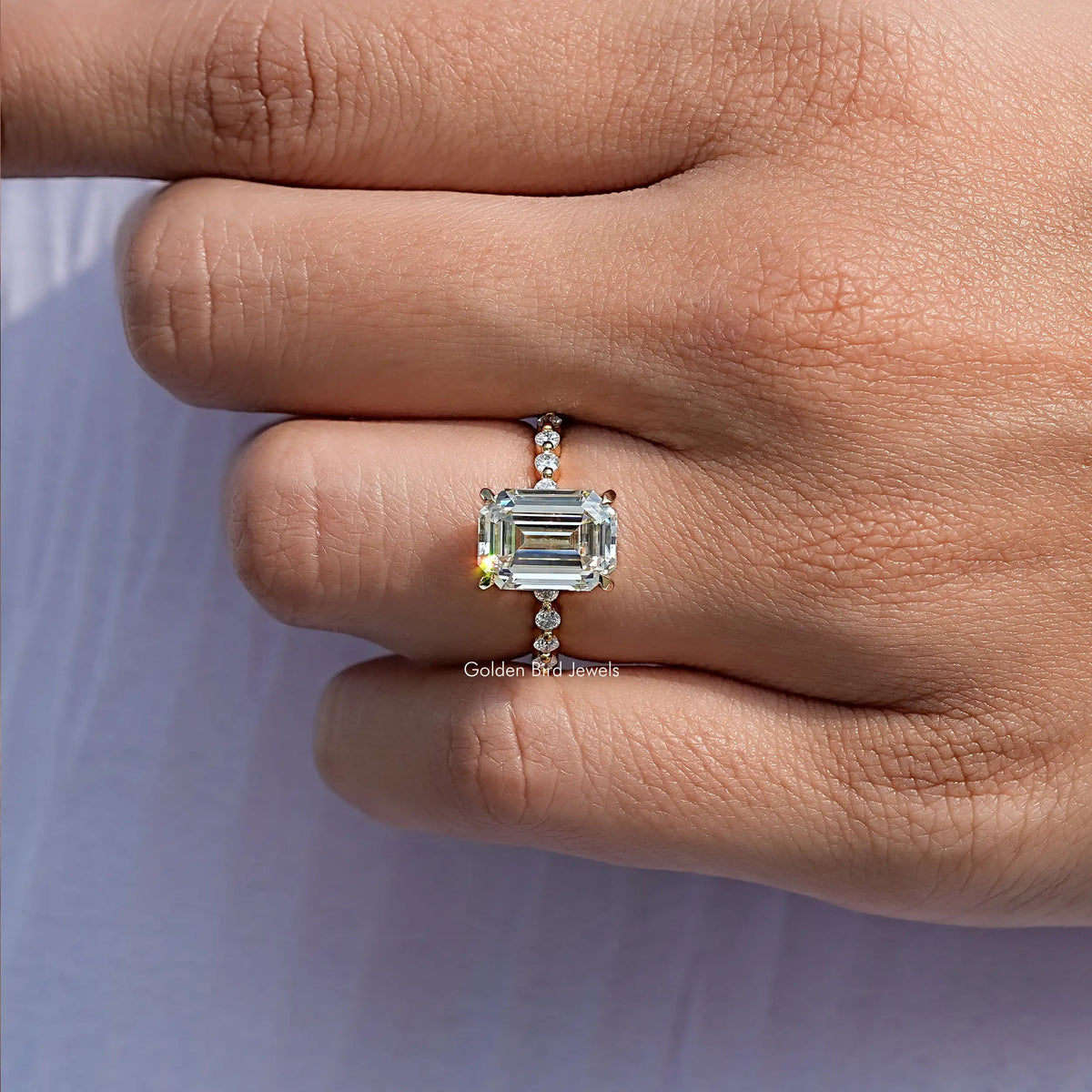 Silver emerald-cut moissanite ring with prong-set center and small side sparkle stones