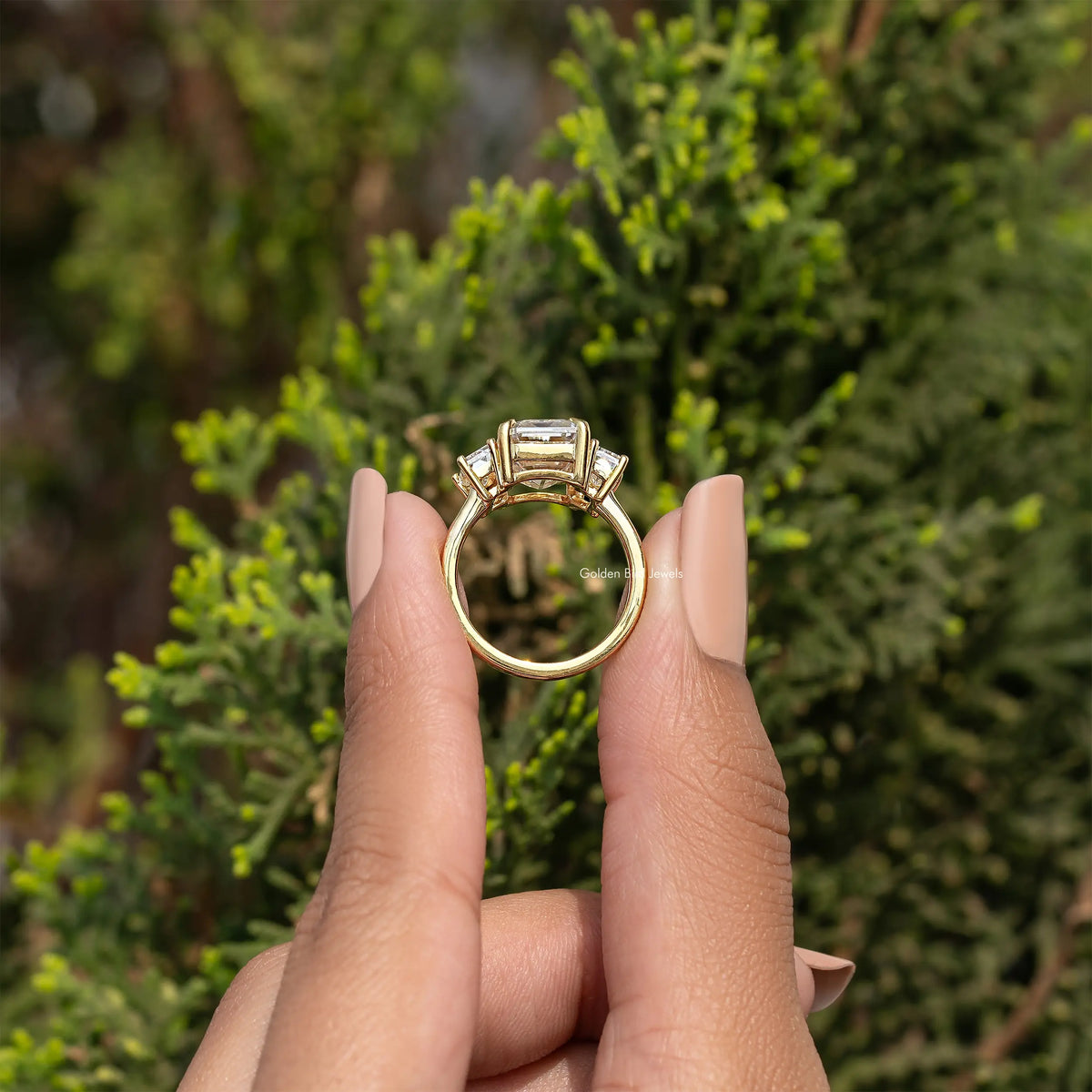 Three-stone emerald-cut moissanite ring viewed from the back, gold-tone setting.