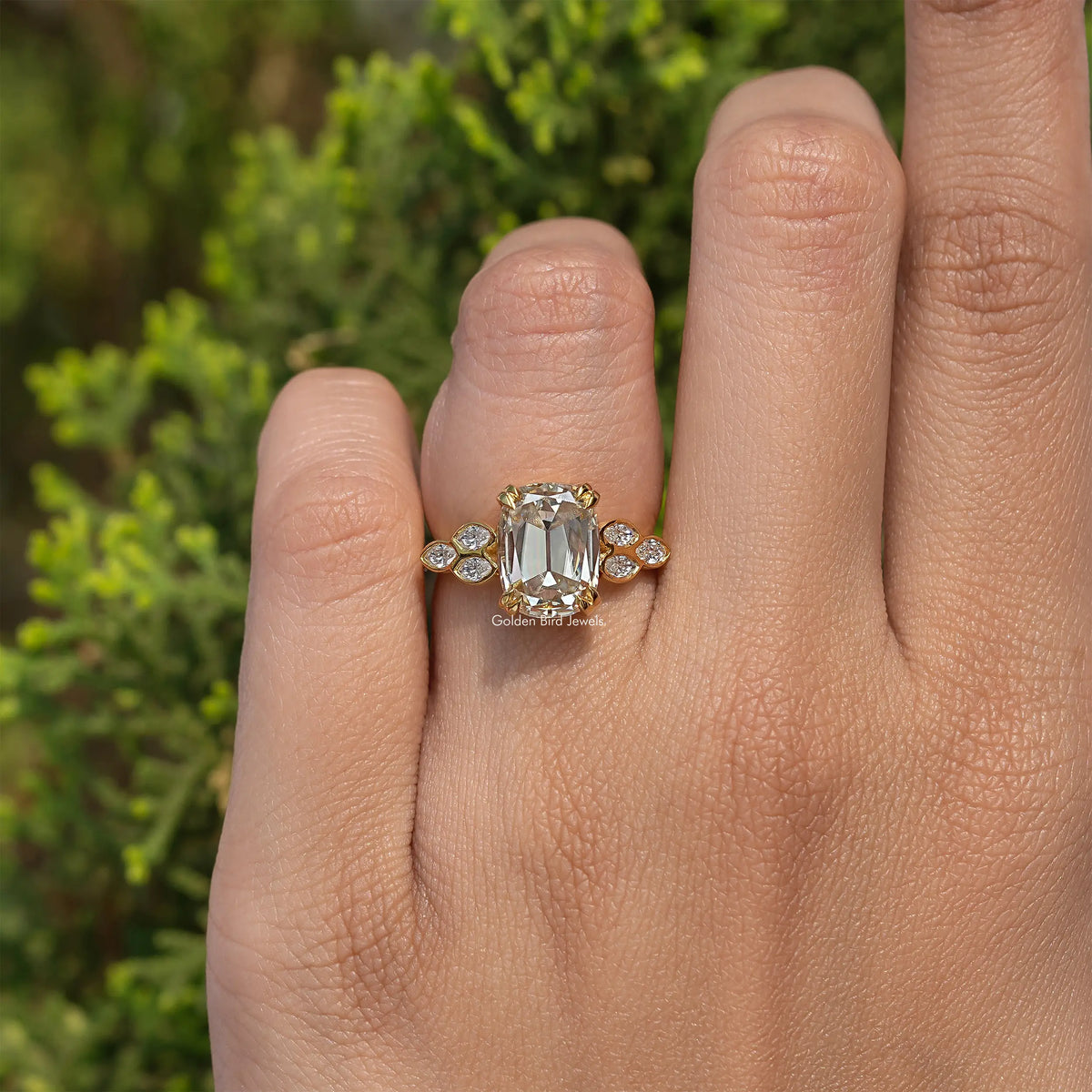 Gold-tone cushion-cut moissanite engagement ring on finger with round side stones