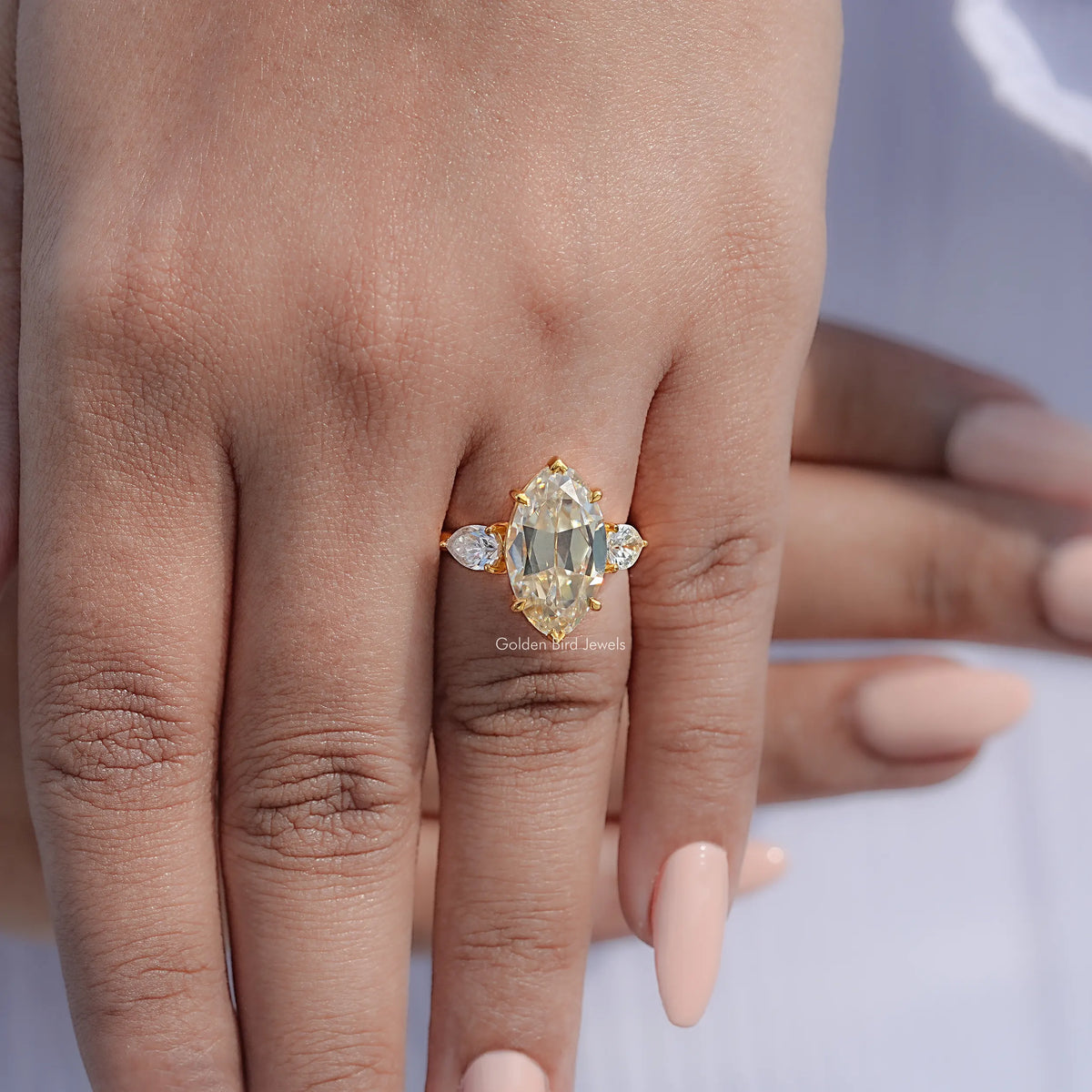 Three-stone pear and round moissanite ring on hand, gold-tone prong setting