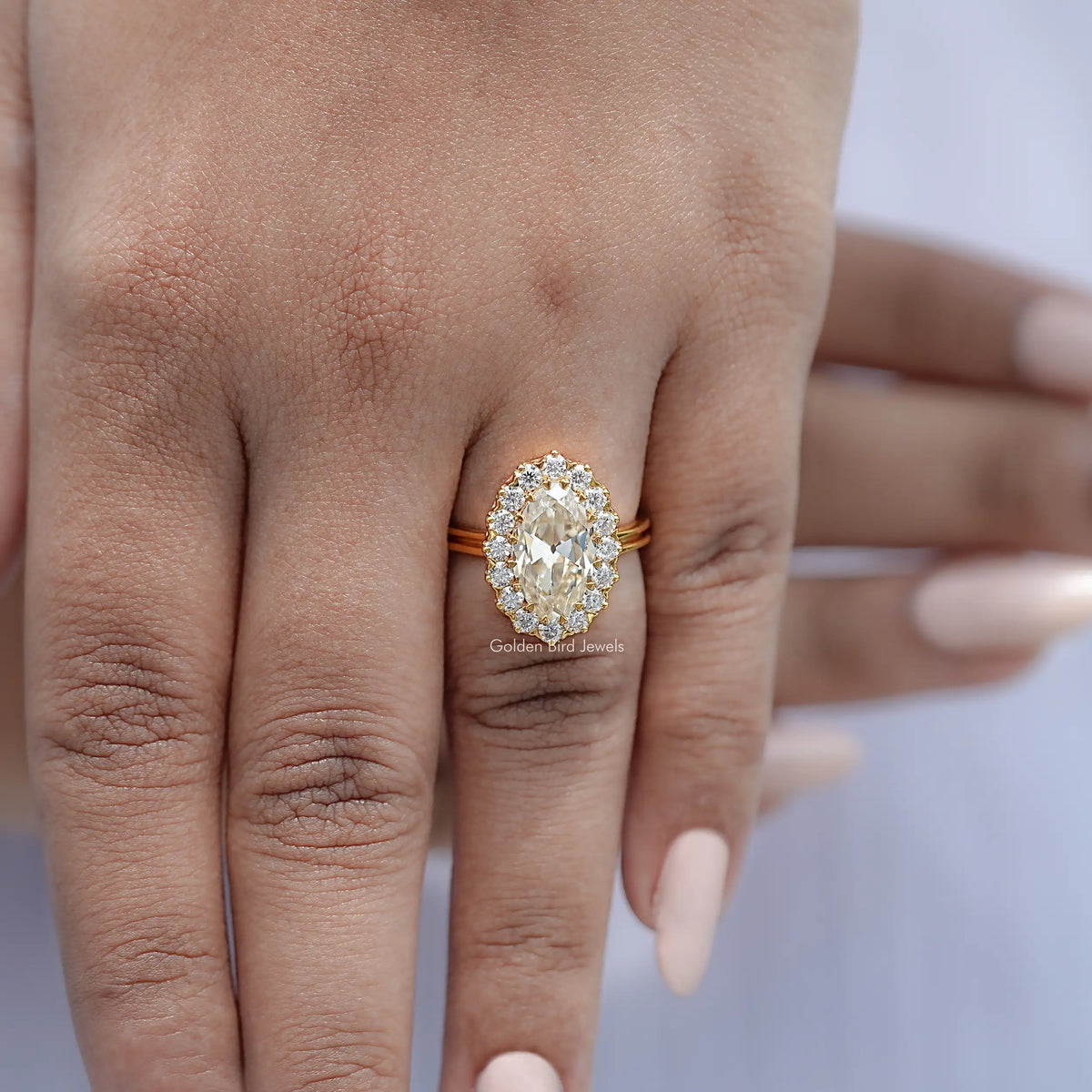 Gold-tone oval moissanite halo ring on hand, band with thin shoulders