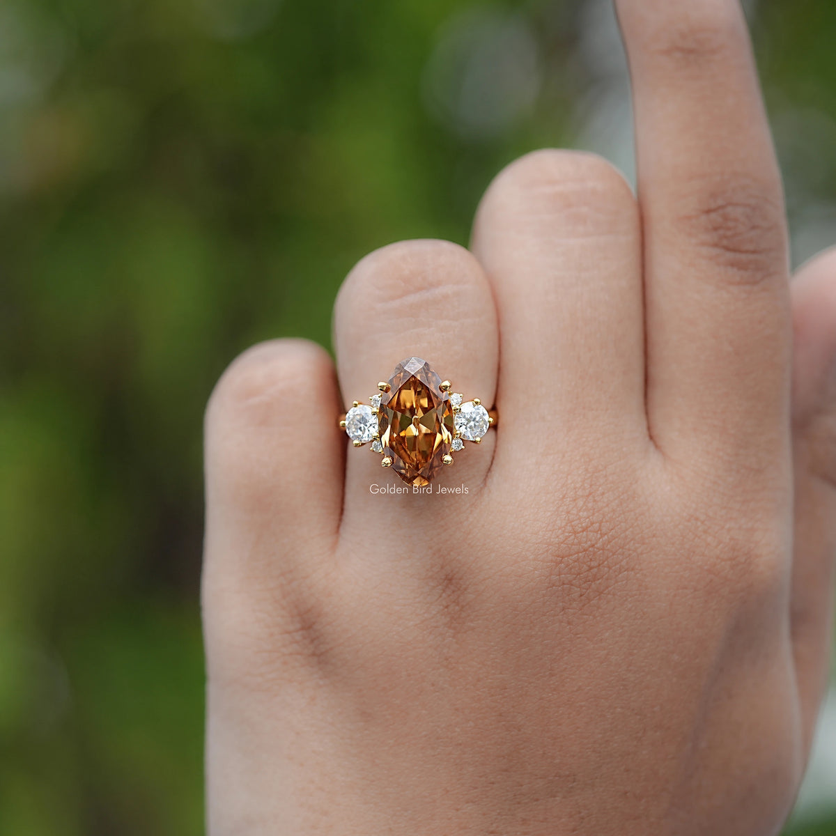 Moissanite engagement ring with oval amber center and two round side stones, gold setting