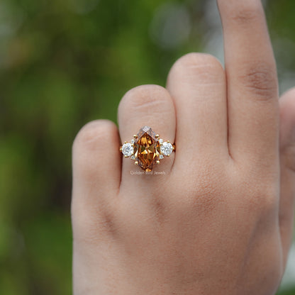 Moissanite engagement ring with oval amber center and two round side stones, gold setting