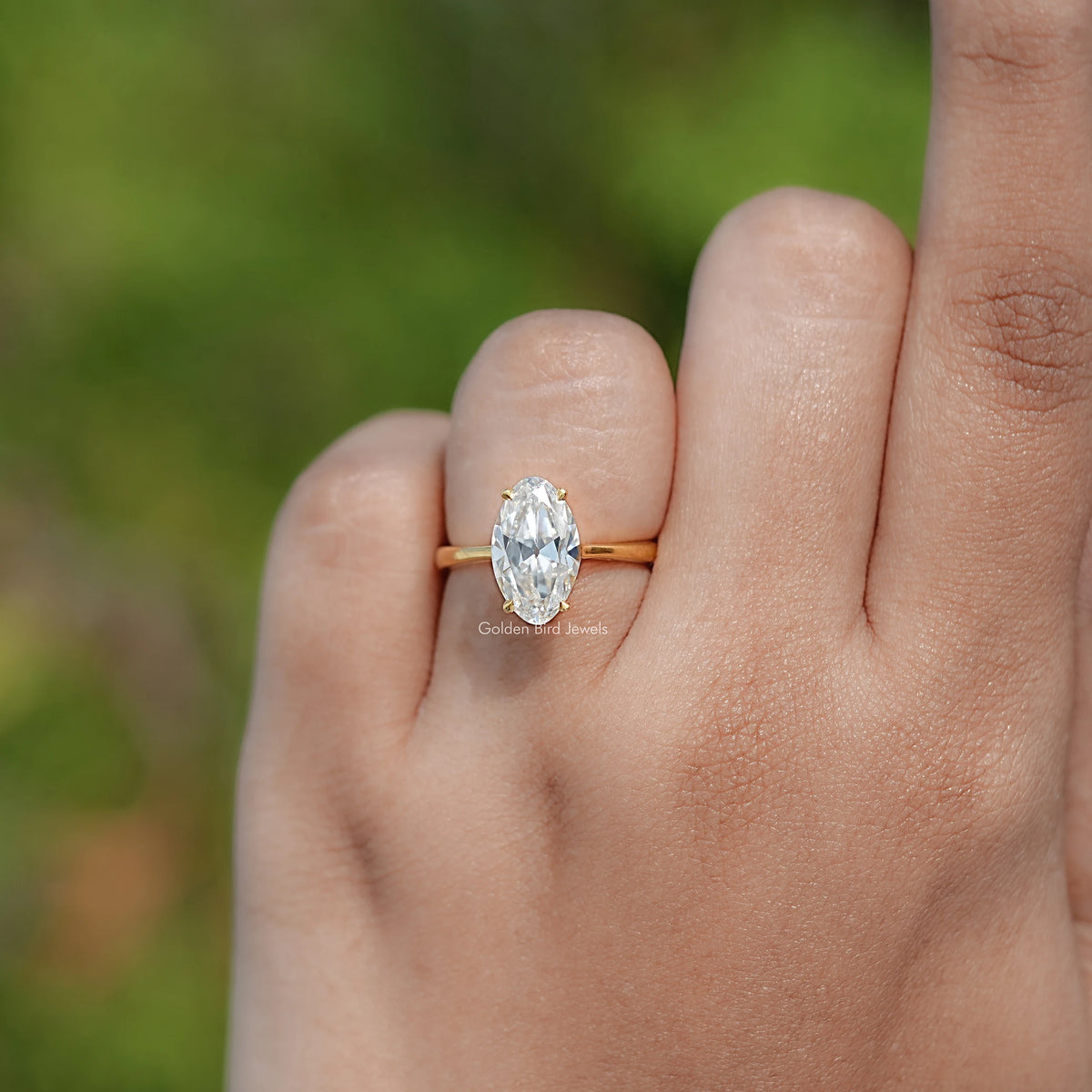 Gold oval moissanite solitaire ring on finger, front close-up