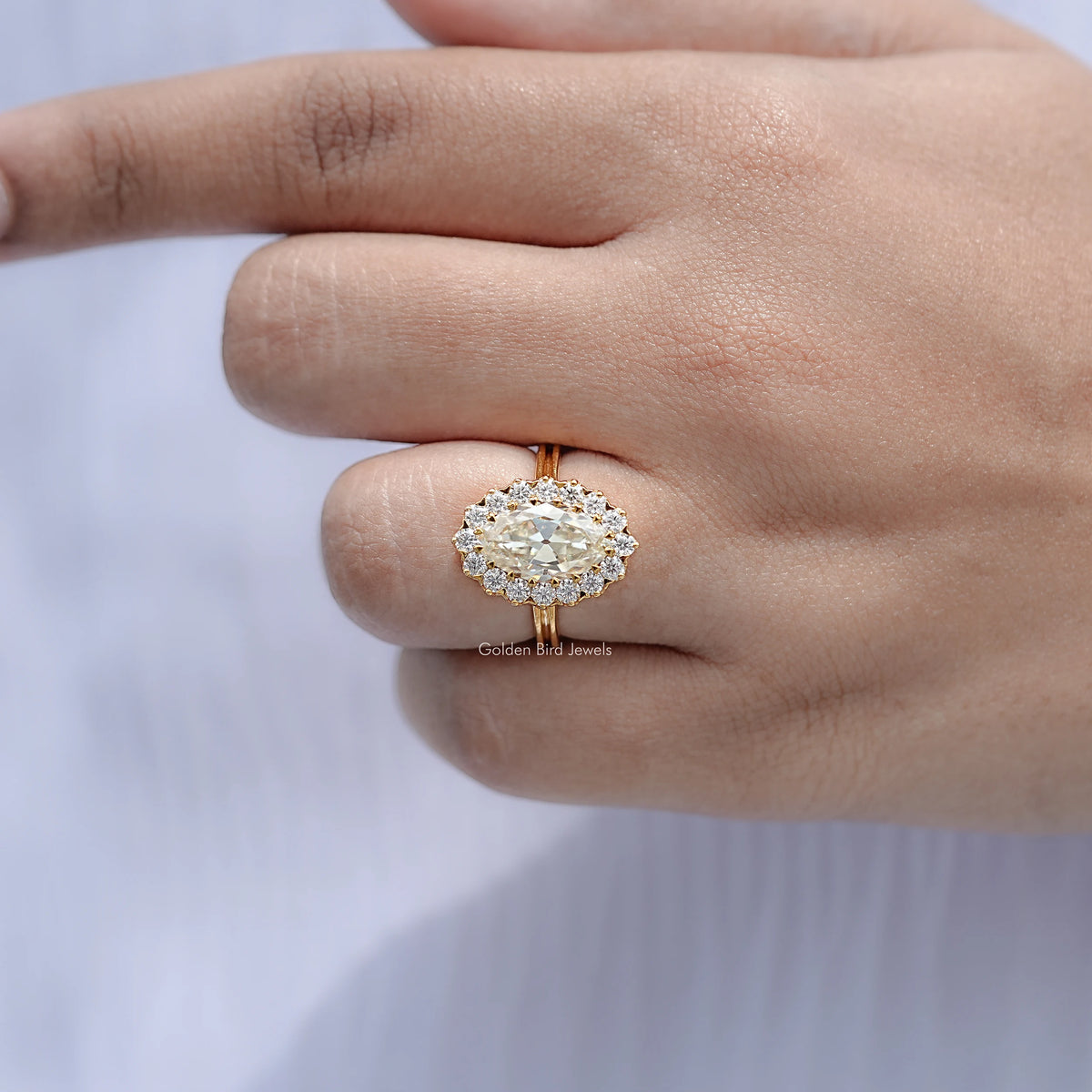 Gold-tone oval moissanite halo engagement ring on open palm, close