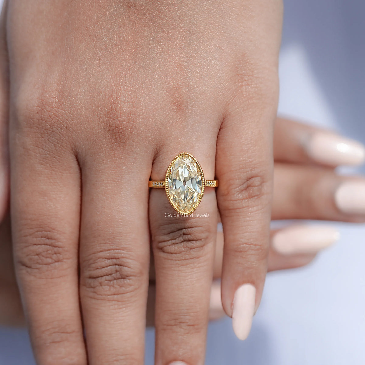 Gold oval moissanite ring on hand, milgrain bezel and slim side band
