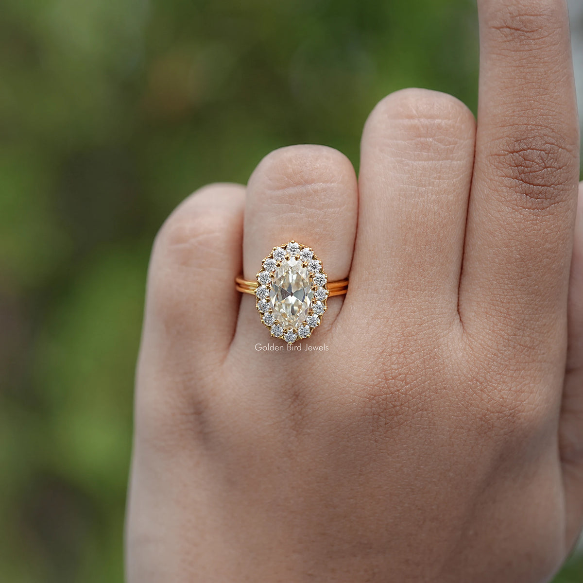 Gold-tone oval moissanite halo engagement ring on hand, close-up