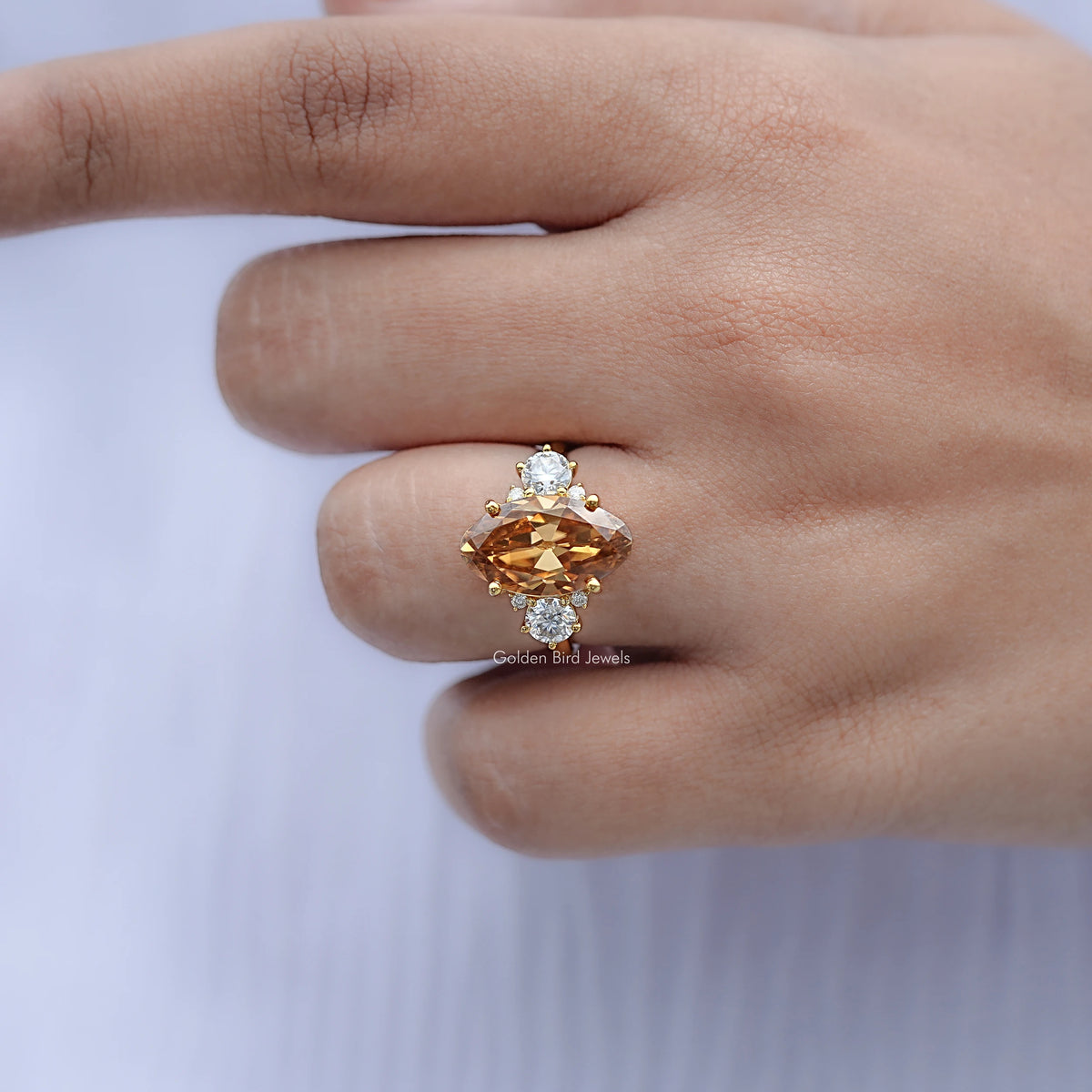 Moissanite engagement ring on finger, oval amber center with four small round accents, gold