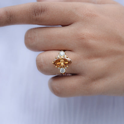 Moissanite engagement ring on finger, oval amber center with four small round accents, gold