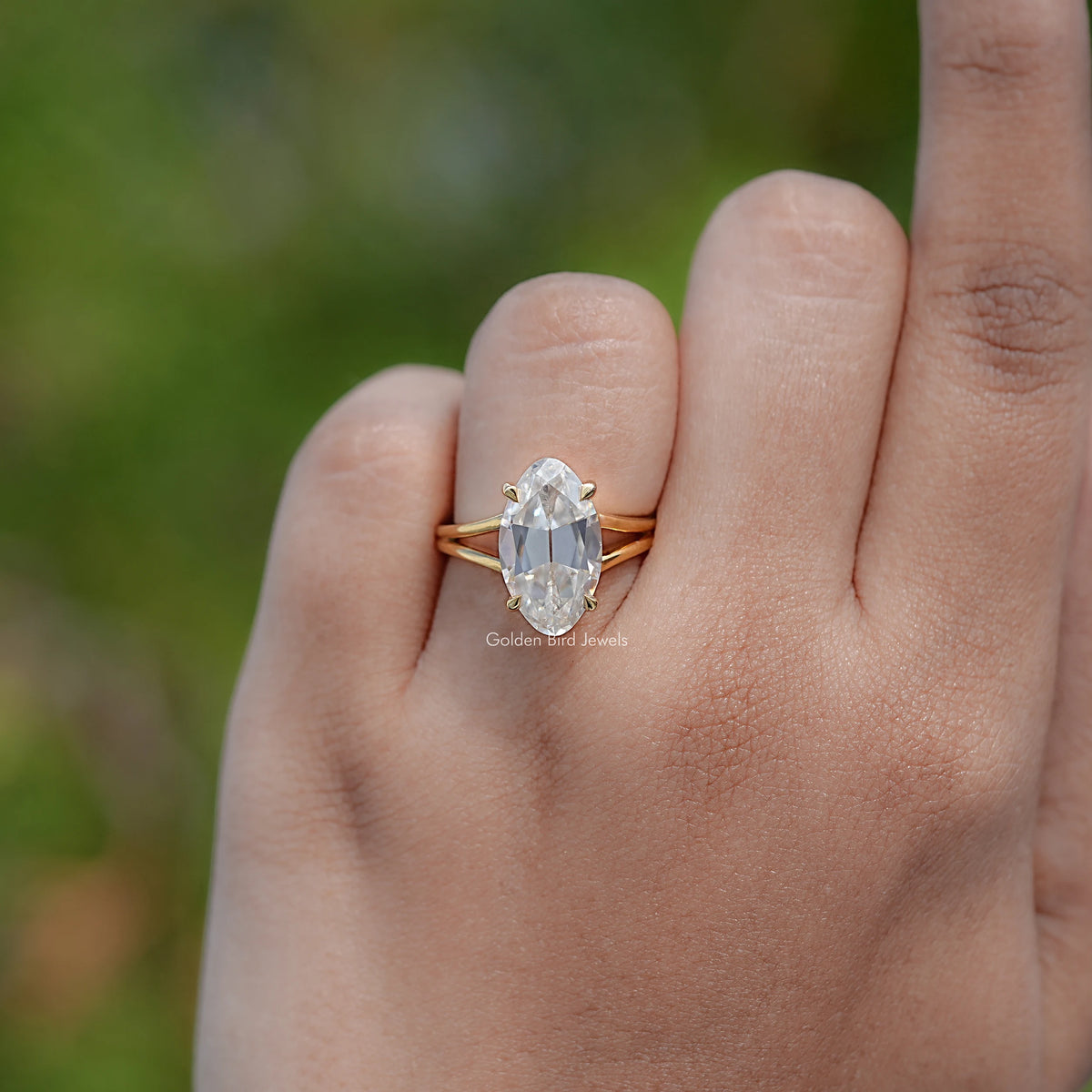 Gold moissanite solitaire ring, oval center stone and split shank on hand