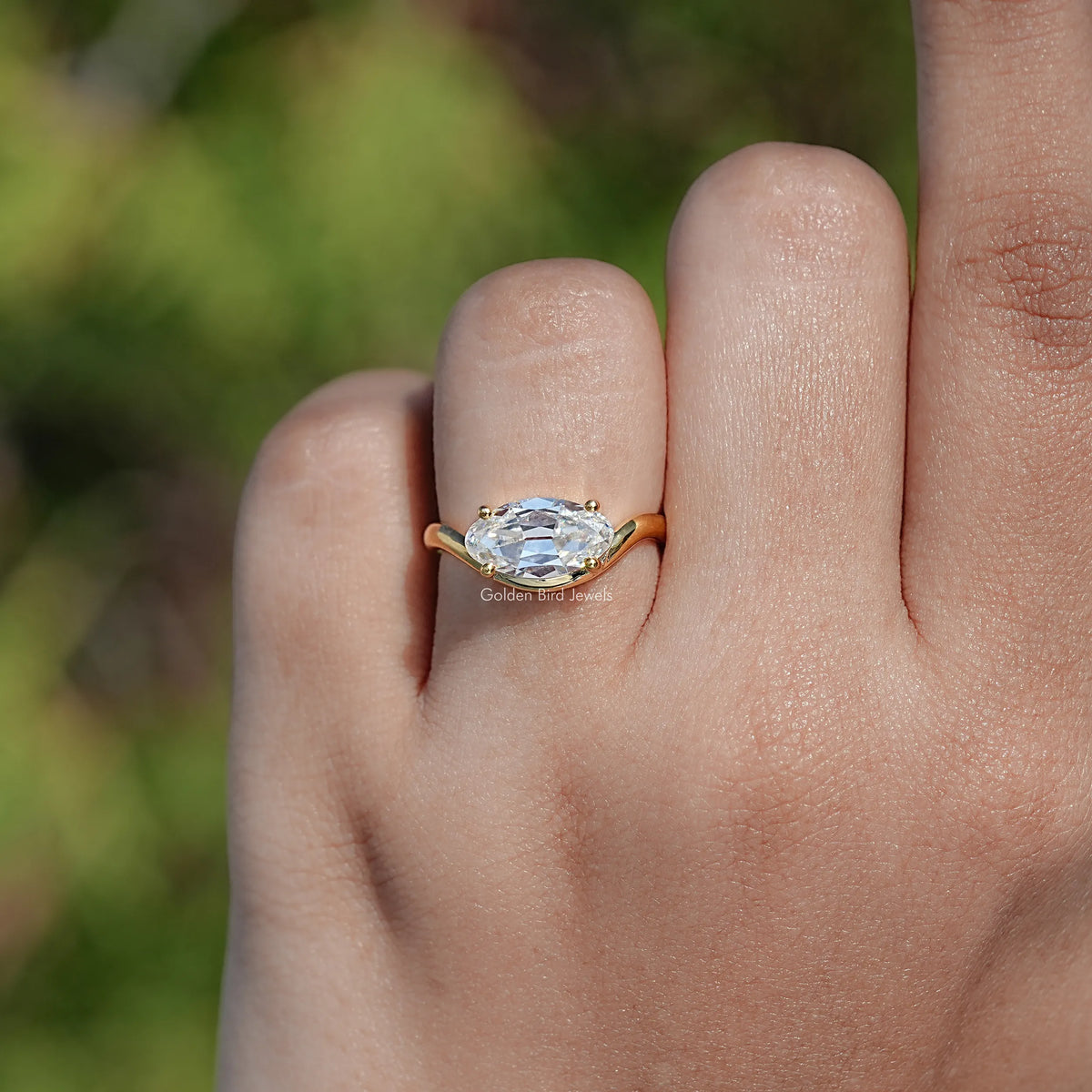 Gold-tone solitaire moissanite ring on finger, oval stone with prongs