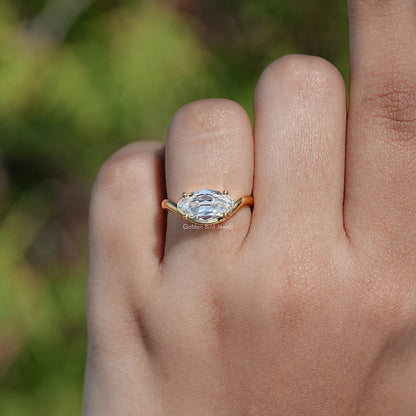 Gold-tone solitaire moissanite ring on finger, oval stone with prongs
