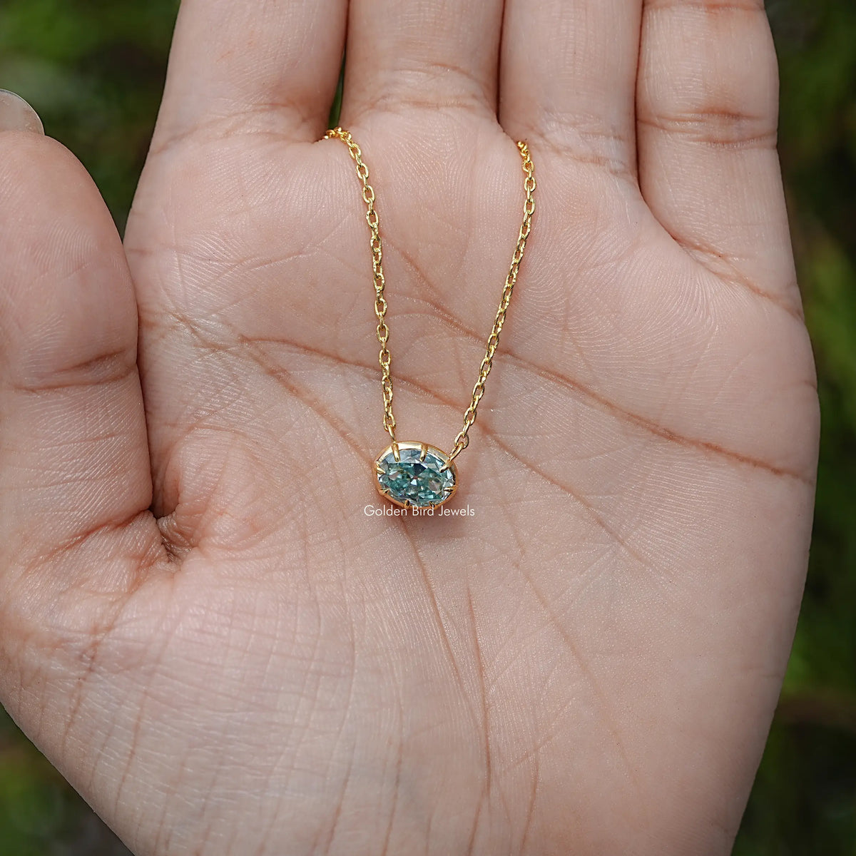 Gold-tone oval moissanite pendant necklace on open palm with blue center stone