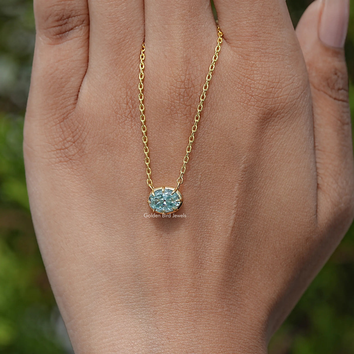 Oval moissanite solitaire pendant necklace on palm with gold-tone chain and blue stone