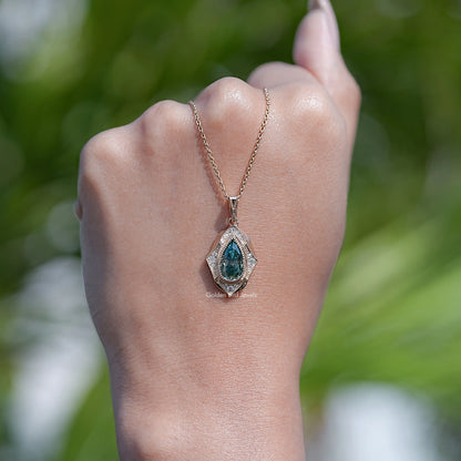 Teal pear-cut moissanite pendant on gold-tone chain against outdoor greenery