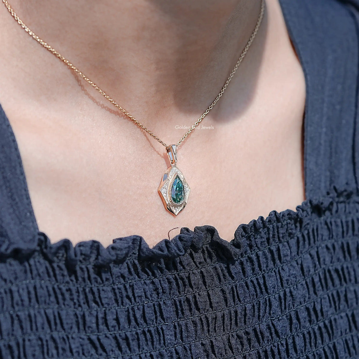 Teal pear-cut moissanite pendant on a fine gold-tone chain over a neckline