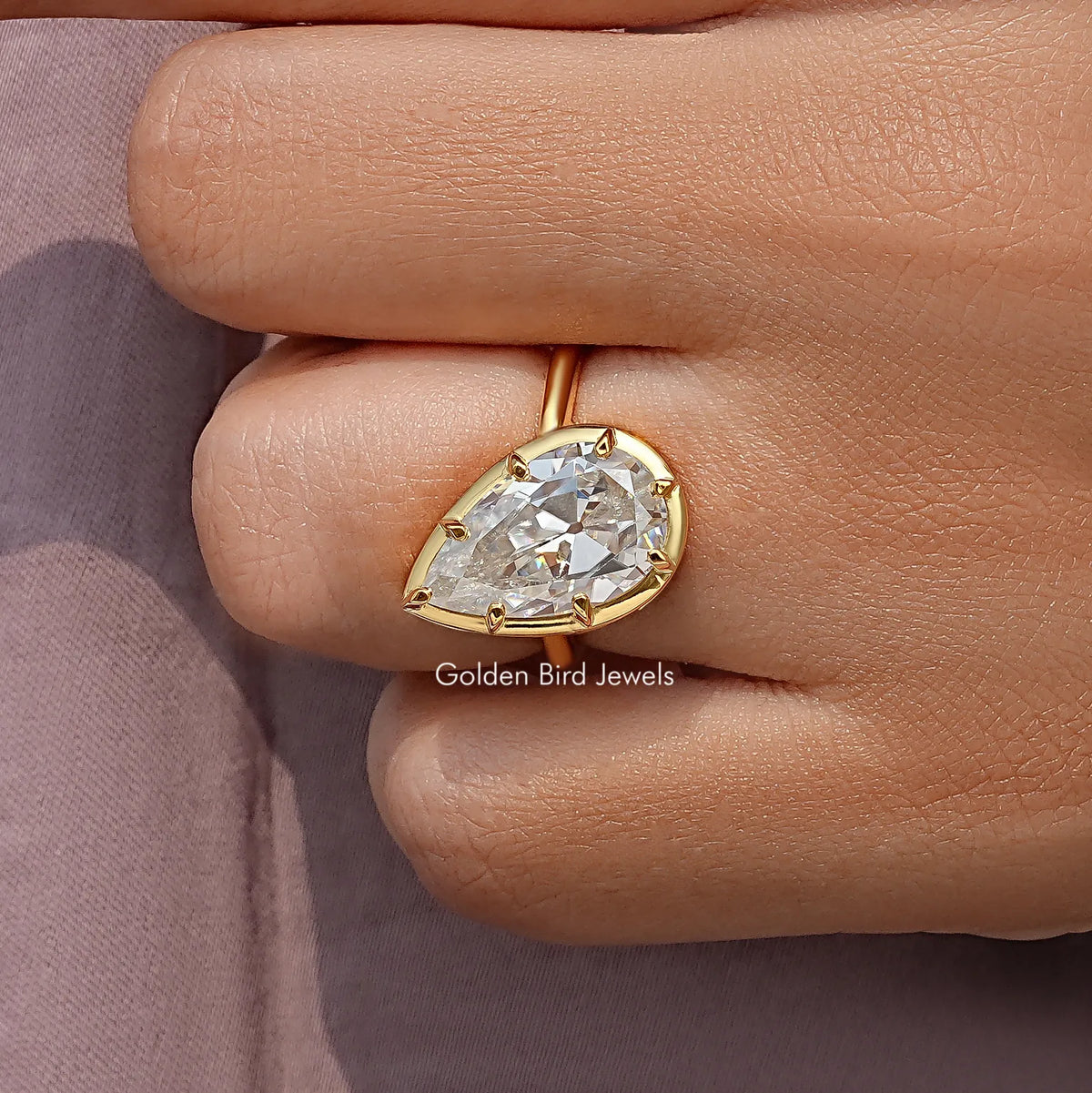 Pear-cut solitaire ring viewed from the side, gold-tone setting with prongs