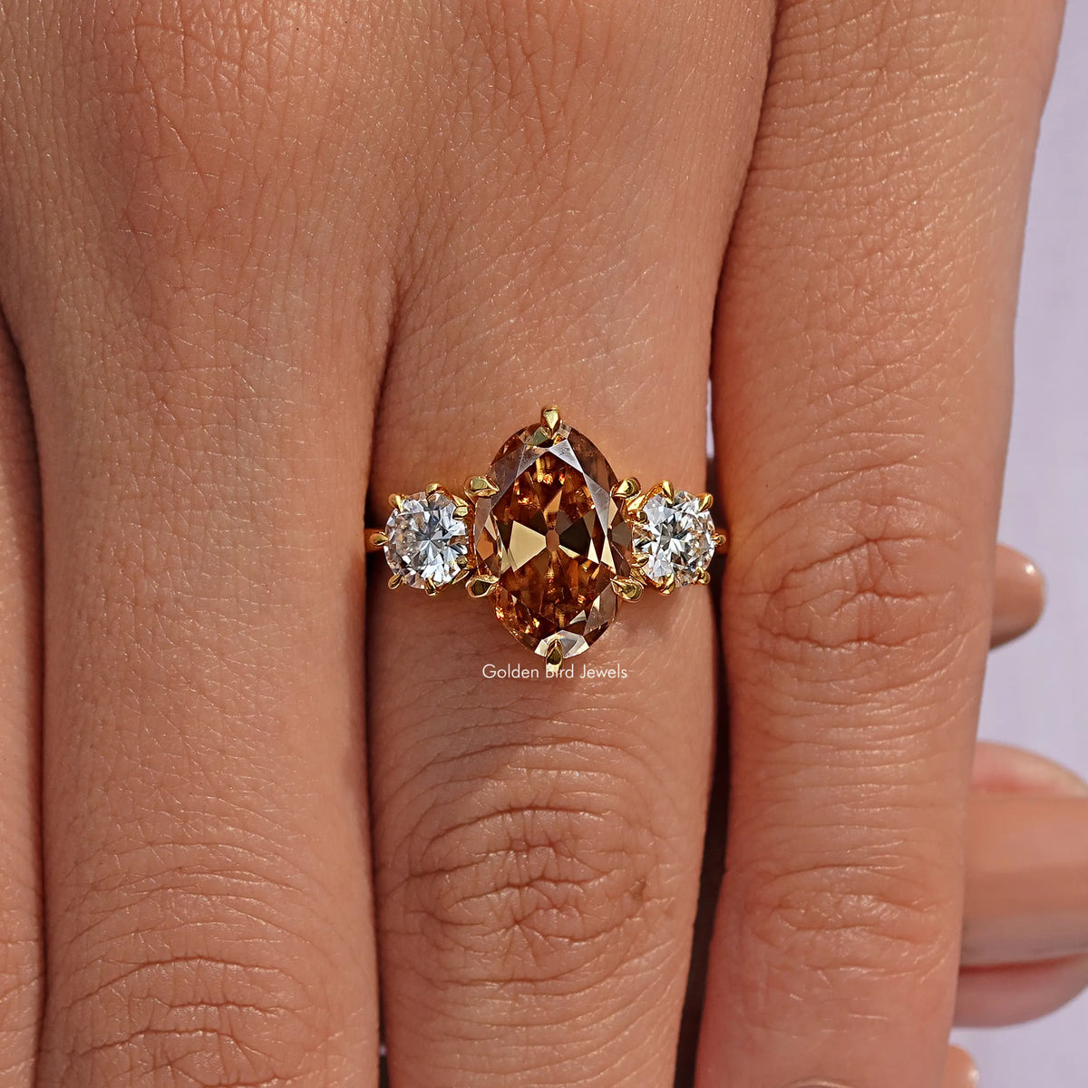 Three-stone oval engagement ring with brown center and round side stones on hand