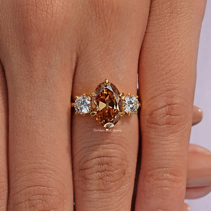 Three-stone oval engagement ring with brown center and round side stones on hand
