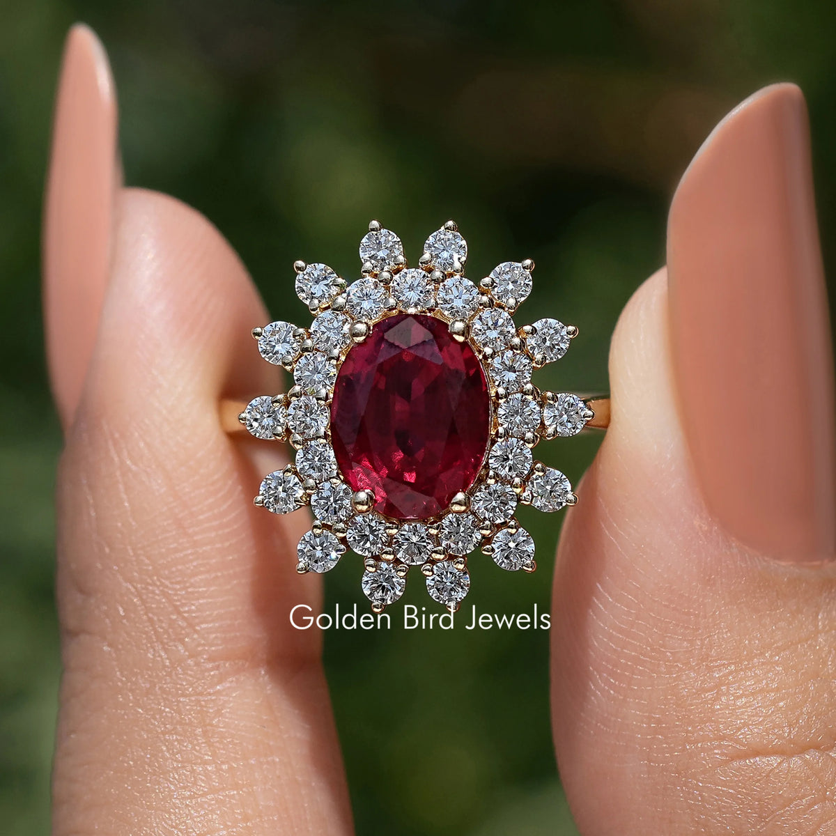 Oval ruby-colored gemstone halo ring with clustered round diamonds on hand