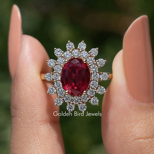 Oval ruby-colored gemstone halo ring with clustered round diamonds on hand