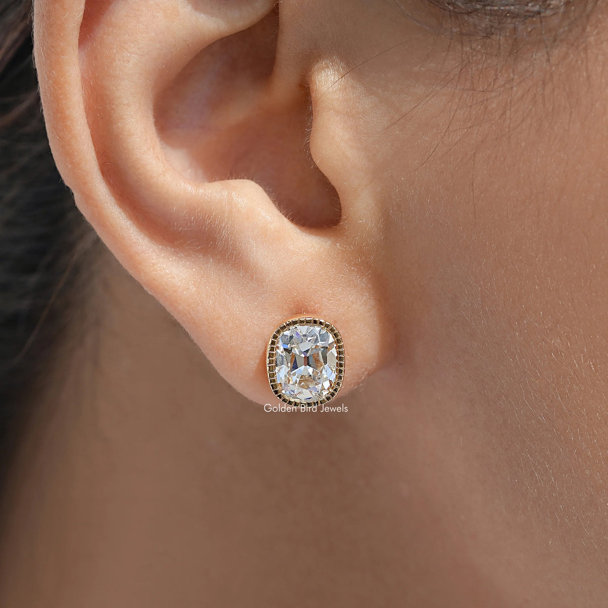 Cushion-cut diamond stud earring with milgrain bezel in gold setting on ear