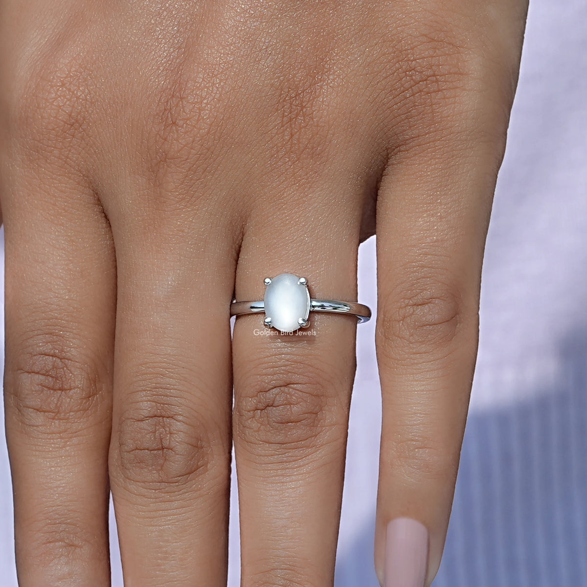 Oval moonstone solitaire ring on hand; light blue oval gem on slim silver band