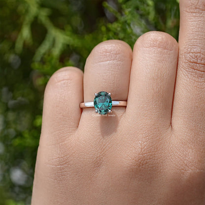 Oval-cut moissanite engagement ring in sterling silver, teal center stone on finger