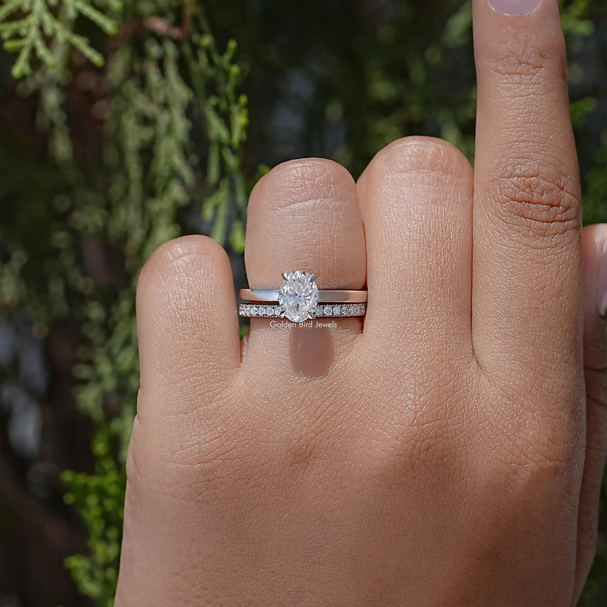 Oval-cut moissanite bridal ring set on finger with matching silver band