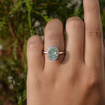 Rose-gold oval moissanite solitaire ring, bezel-set center stone on finger