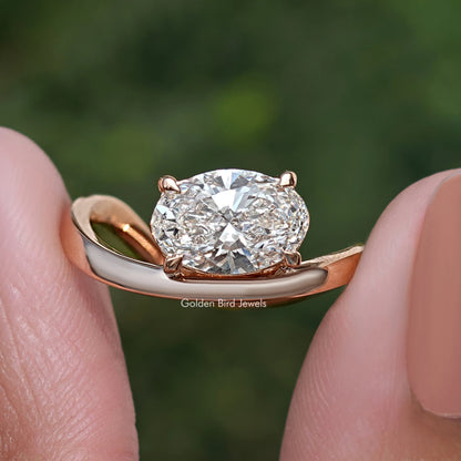 Close-up of oval solitaire diamond ring with rose-gold curved band and prongs