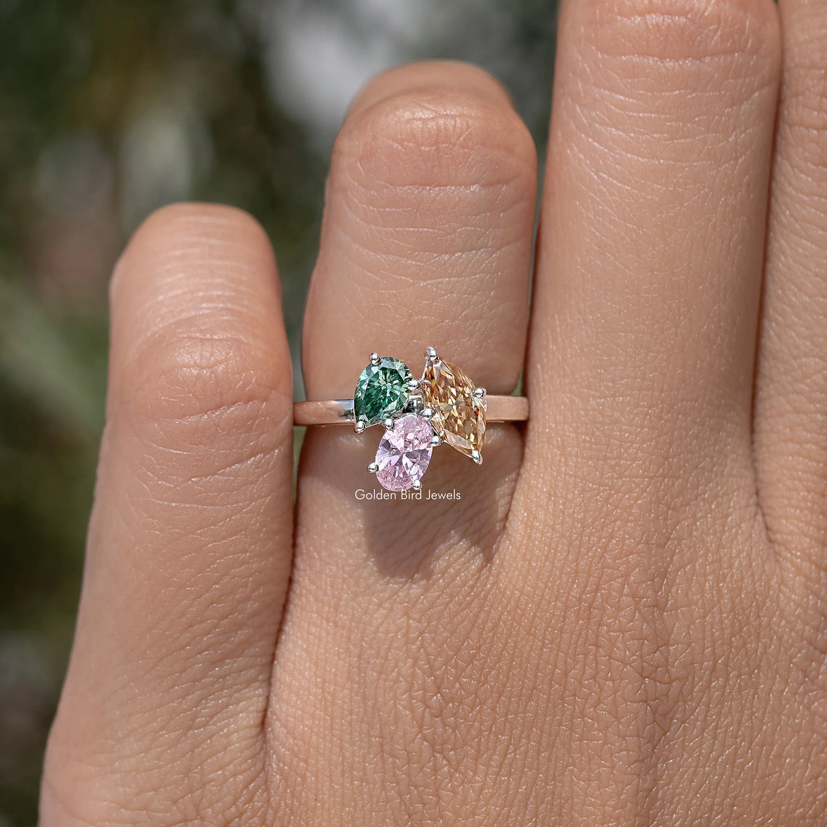 Three-stone engagement ring with green, pink, and amber gemstones in a row