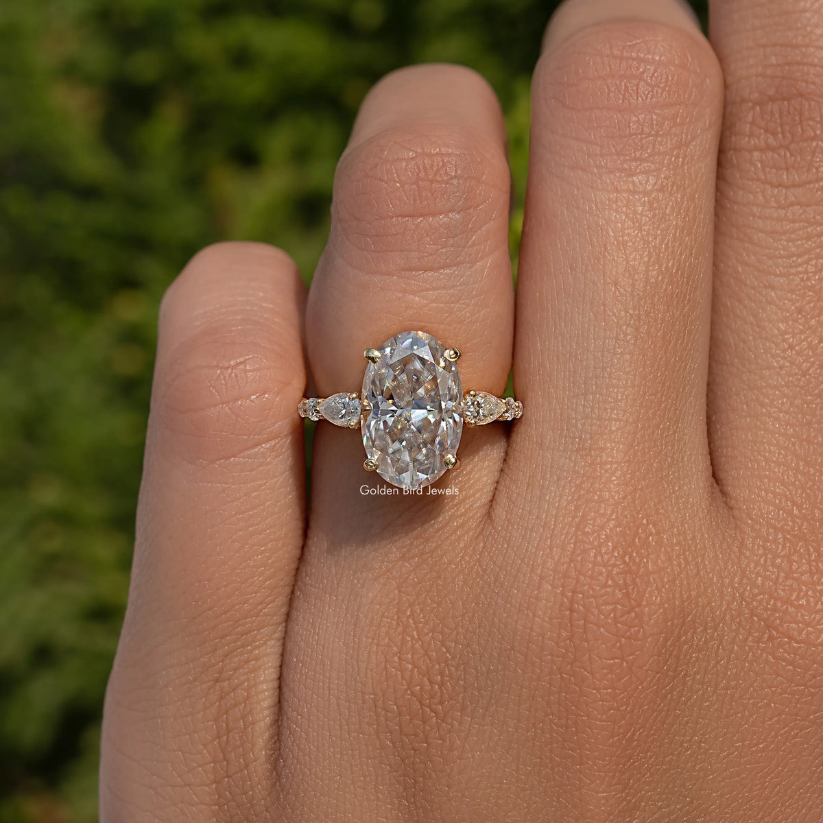 Oval moissanite cluster engagement ring on hand with three-stone side marquise accents