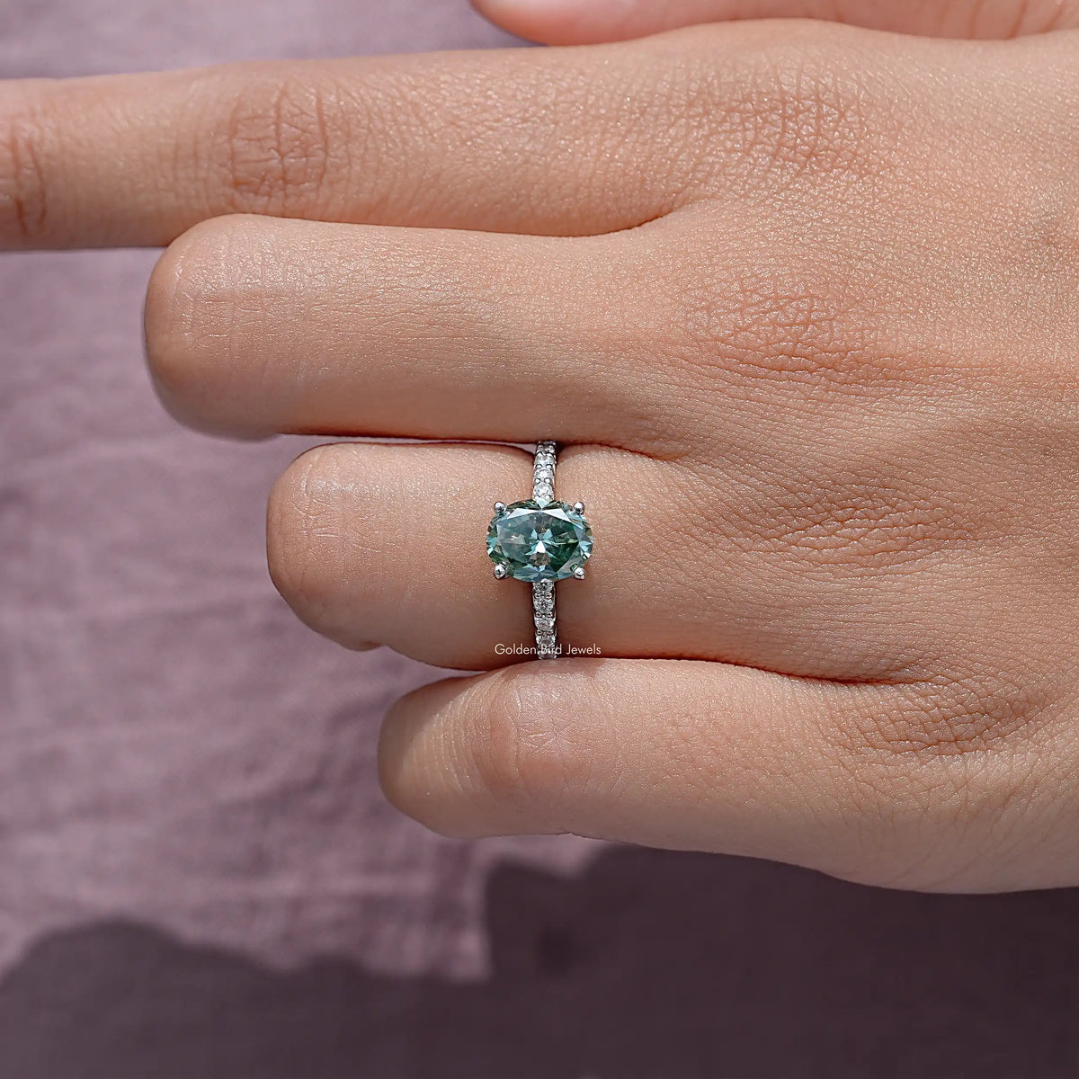 Teal oval center moissanite solitaire ring in 925 silver, side view on hand