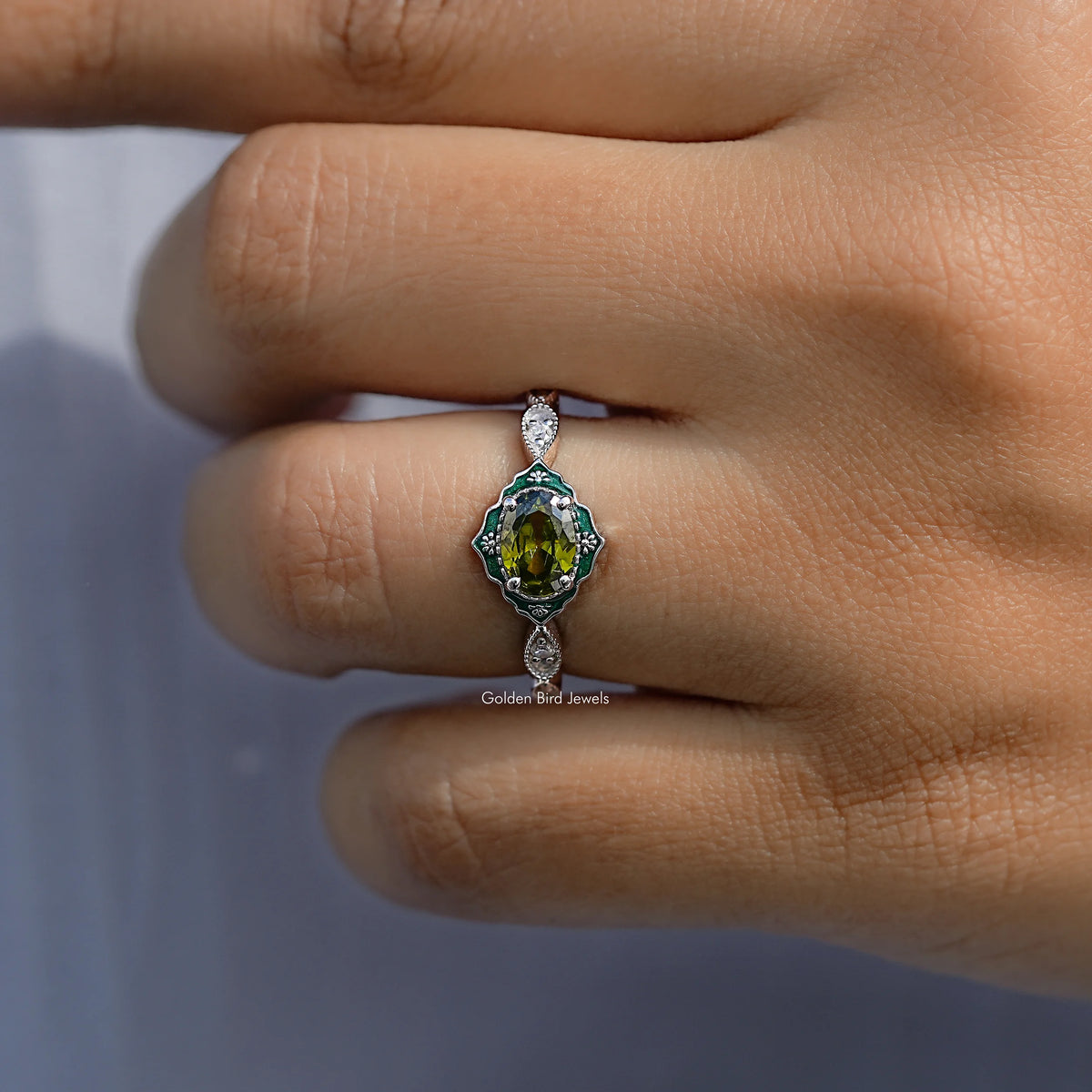 Halo engagement ring featuring an oval green center stone with two round diamond accents