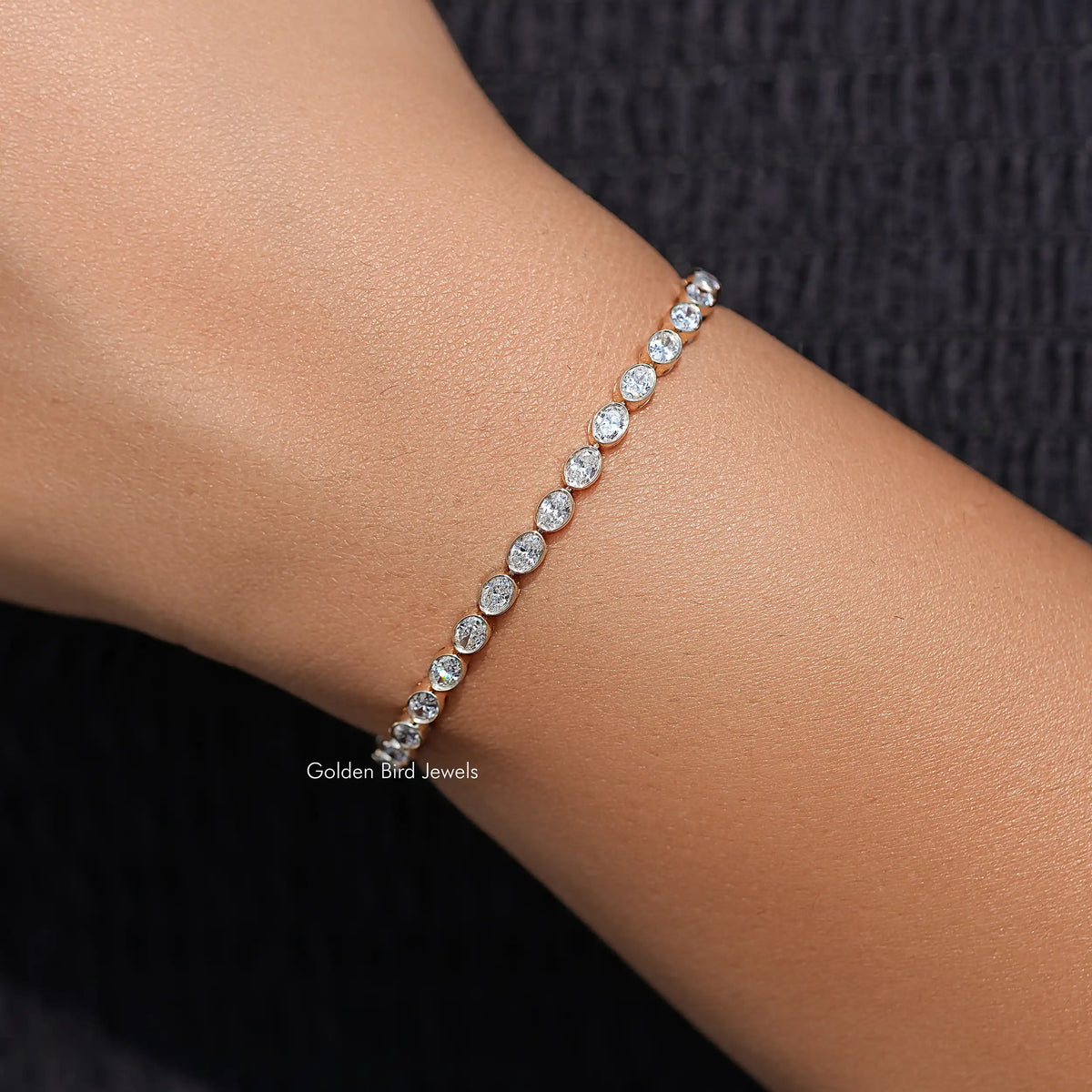 Silver-tone oval diamond tennis bracelet on wrist, evenly spaced oval-cut stones