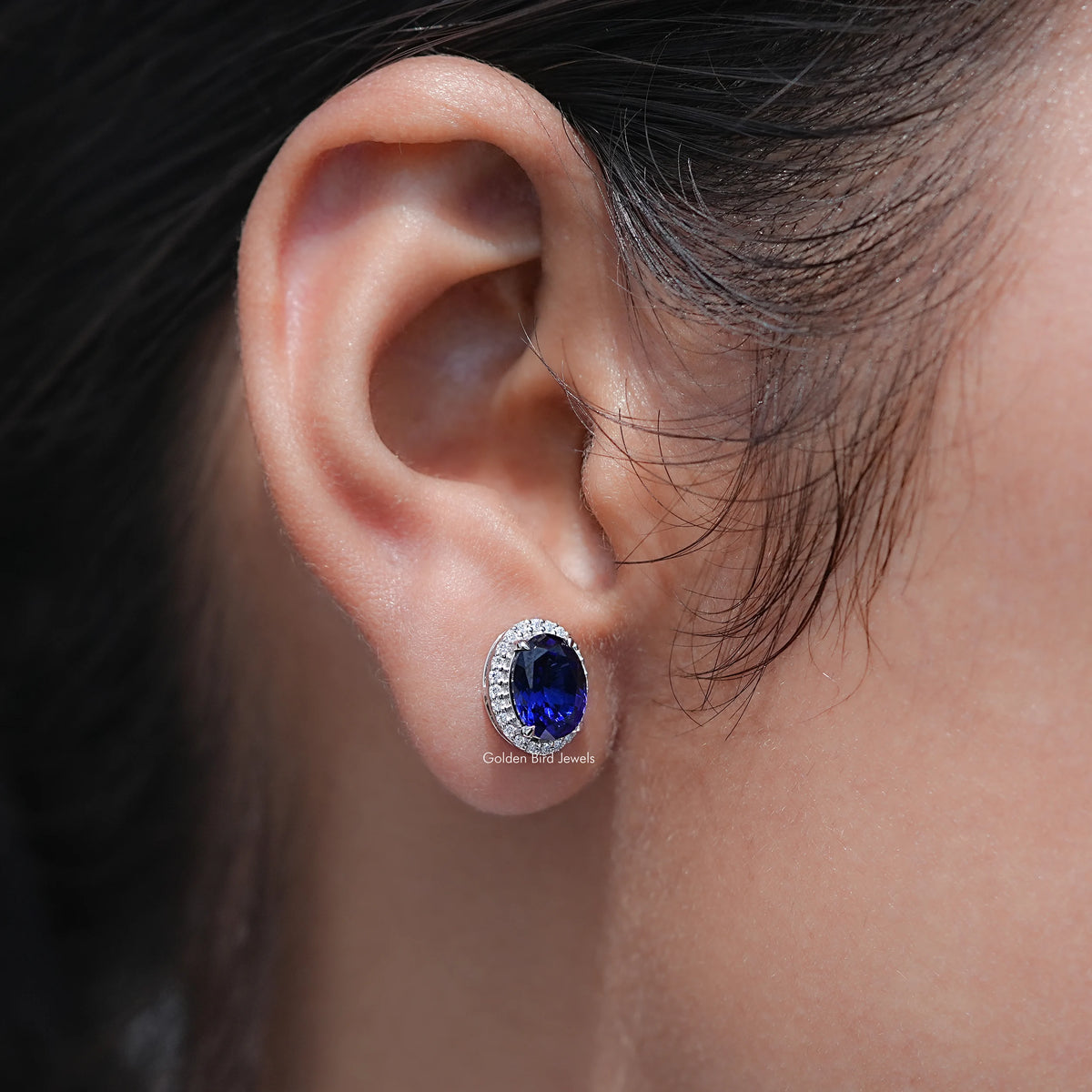 Oval blue gemstone halo stud earring, side view on ear with halo detail